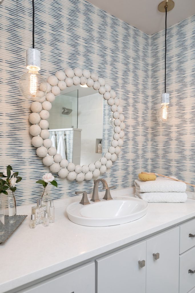 White and Blue Bathroom with wallpaper and white mirror - glass modern pendants - white counter tops with grey cabinets - Scandinavian design